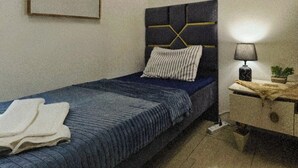 A bedroom with a bed, bedside table, lamp, and a framed picture on the wall.