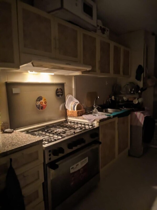A kitchen with a gas stove, oven, cabinets, and a microwave.