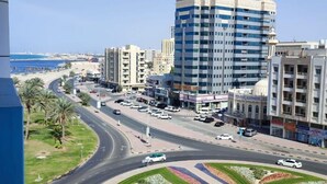A cityscape with a roundabout, buildings, and a beach in the background.