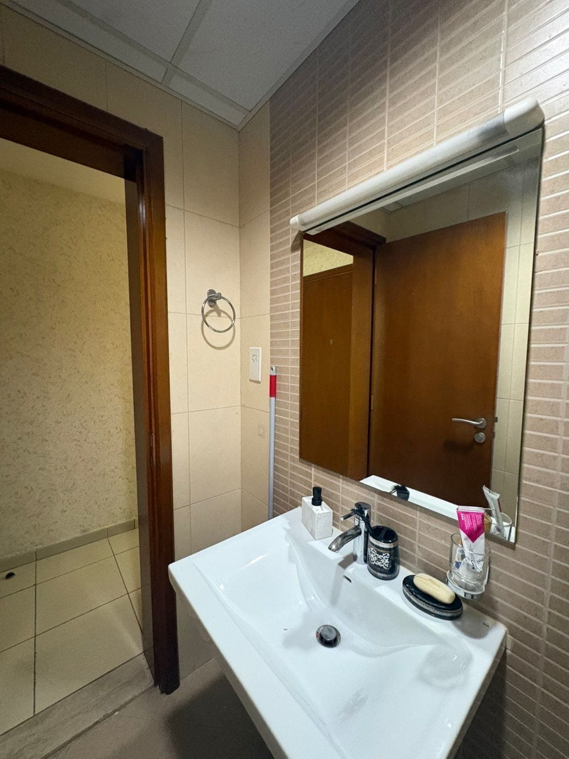 Une salle de bain avec un lavabo blanc, un miroir, un porte-serviette et une porte.