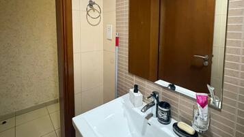 Une salle de bain avec un lavabo blanc, un miroir, un porte-serviette et une porte.