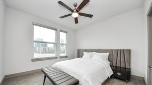 A bedroom with a bed, bench, ceiling fan, and windows with a city view. - Prime Houston 2BR/2BA Galleria + RiverOaks Location (Houston)