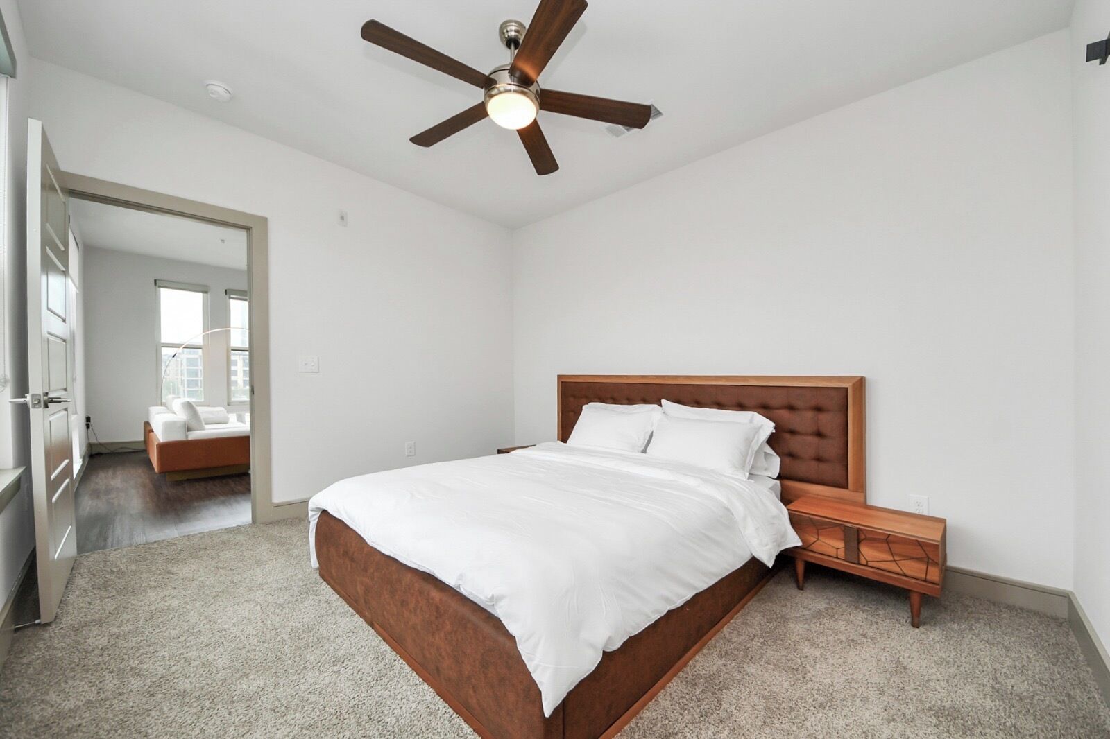 A bedroom with a bed, wooden headboard, nightstand, and a ceiling fan.