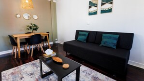 Un salon avec un canapé noir, une table à manger en bois et des chaises. On y trouve une petite table sur laquelle sont posés un bol et une plante.