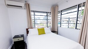 Une chambre d’hôtel avec un lit, une table de chevet, un appareil de climatisation et une fenêtre avec des rideaux.