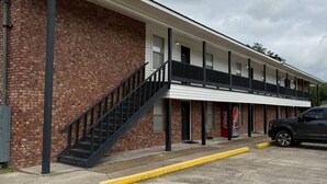 A two-story building with a brick facade, a set of stairs leading to a balcony, and a parked vehicle in the foreground. - Contractor / Plant Workers Specialty (Sulphur)