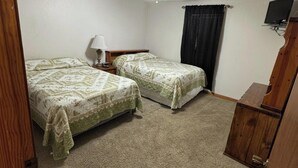 A bedroom with two beds, a ceiling fan, a lamp, a TV, and a wooden cabinet. - Contractor / Plant Workers Specialty (Sulphur)