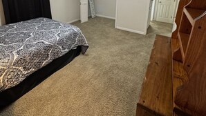 Un dormitorio con cama, ventilador de techo, televisor, cómoda de madera y una puerta.