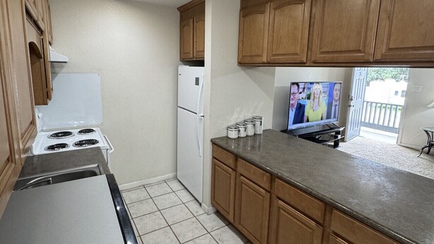 Una cocina con armarios de madera, estufa, refrigerador y televisor.