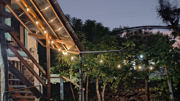 Ein modernes Gebäude mit einer Holztreppe, Lichterketten und einem Garten mit Bäumen und einer Steinmauer.