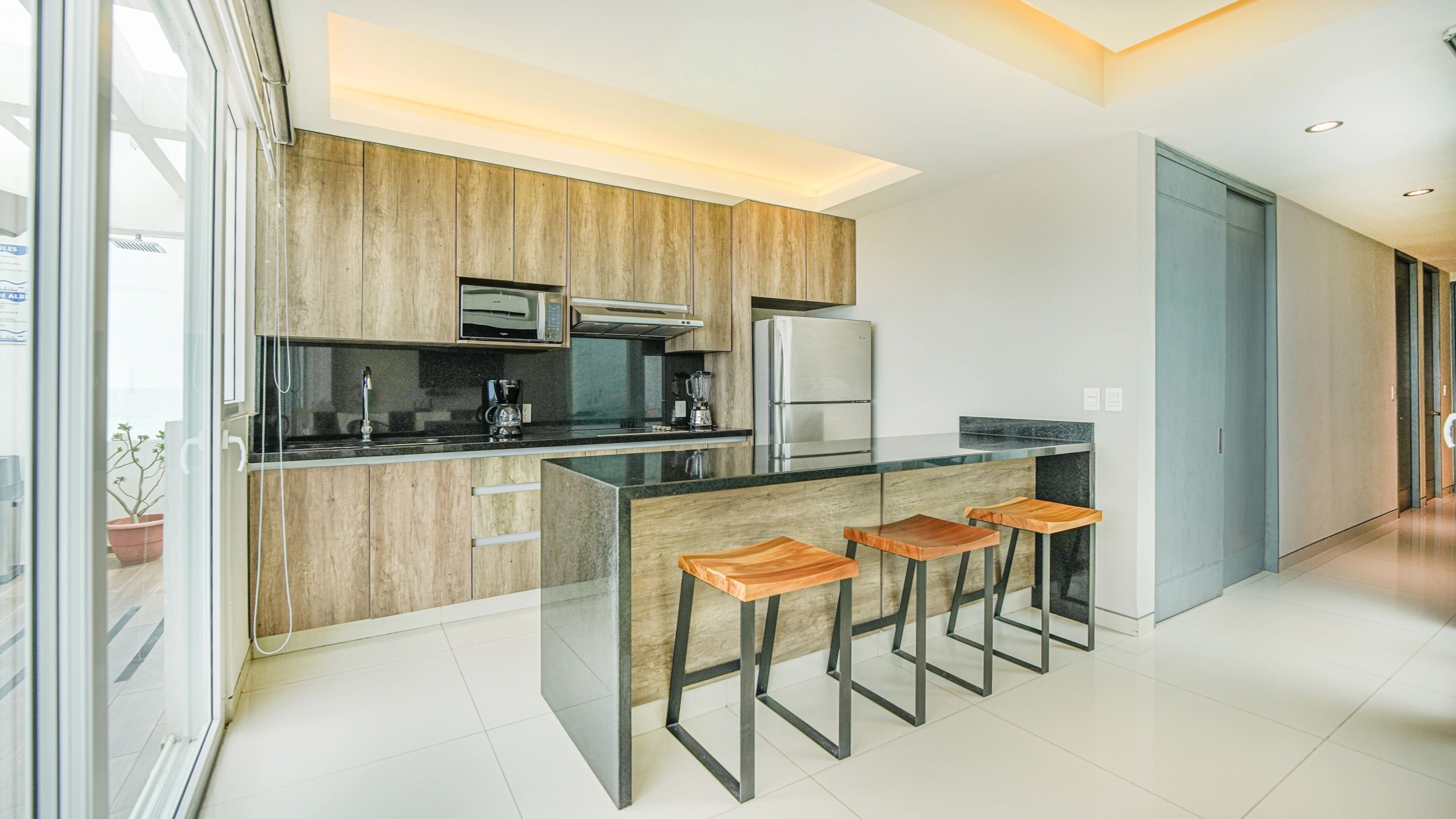 A modern kitchen with wooden cabinets, a black countertop, and a built-in island with bar stools.