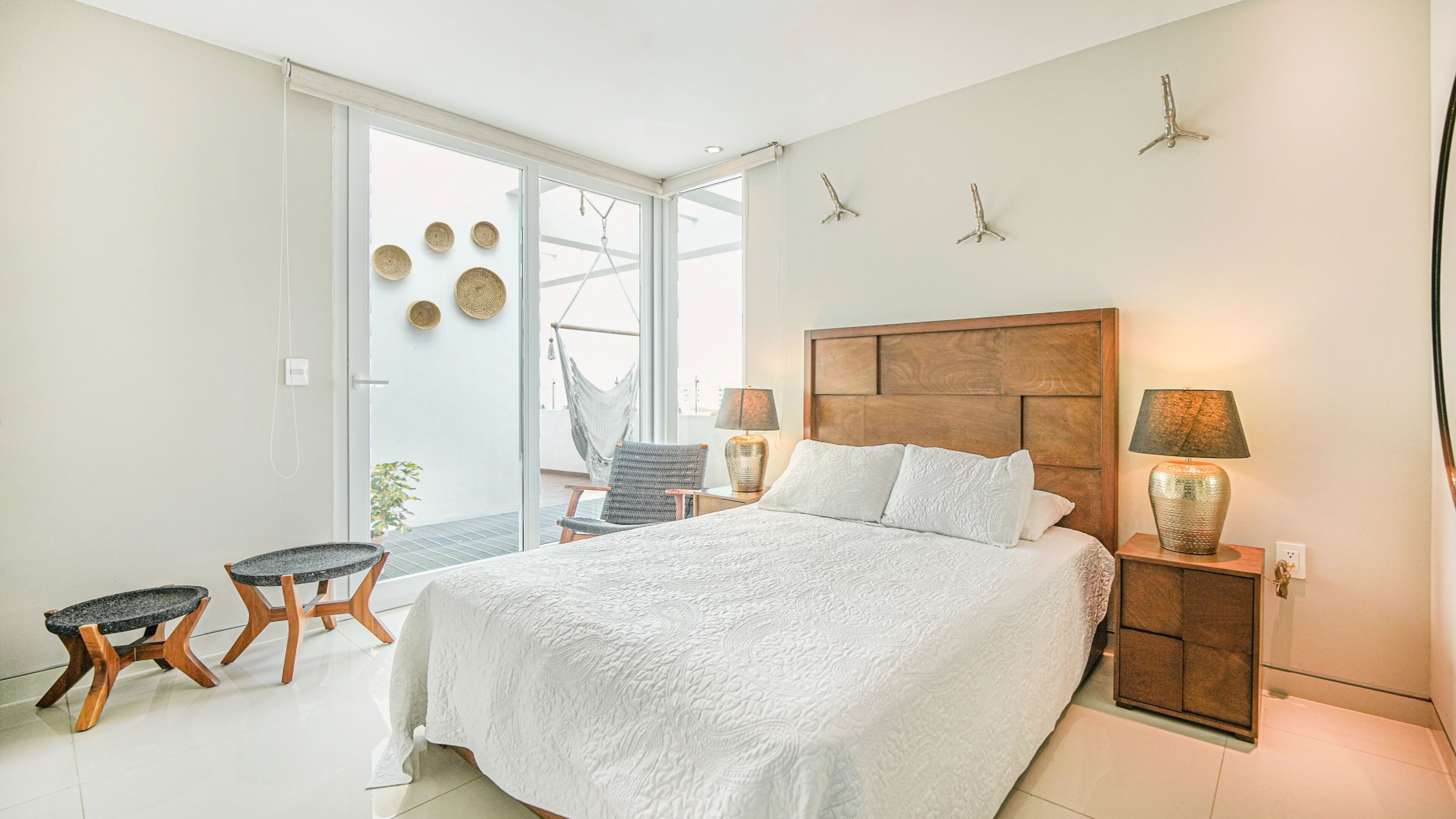 A bedroom with a large bed, two nightstands, a chair, a small table, and a hammock.