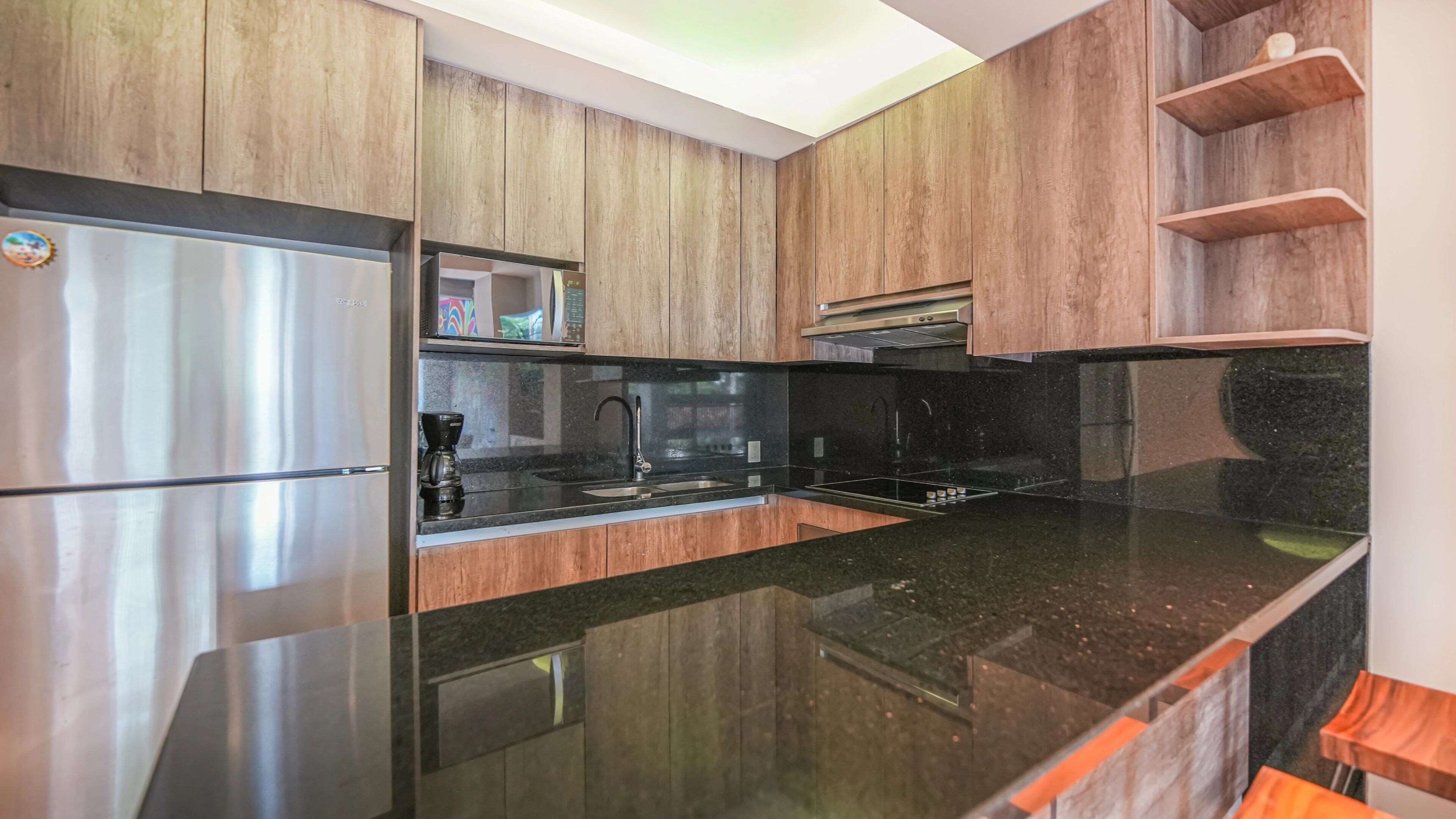 A modern kitchen with wooden cabinets, stainless steel appliances, and a black granite countertop.