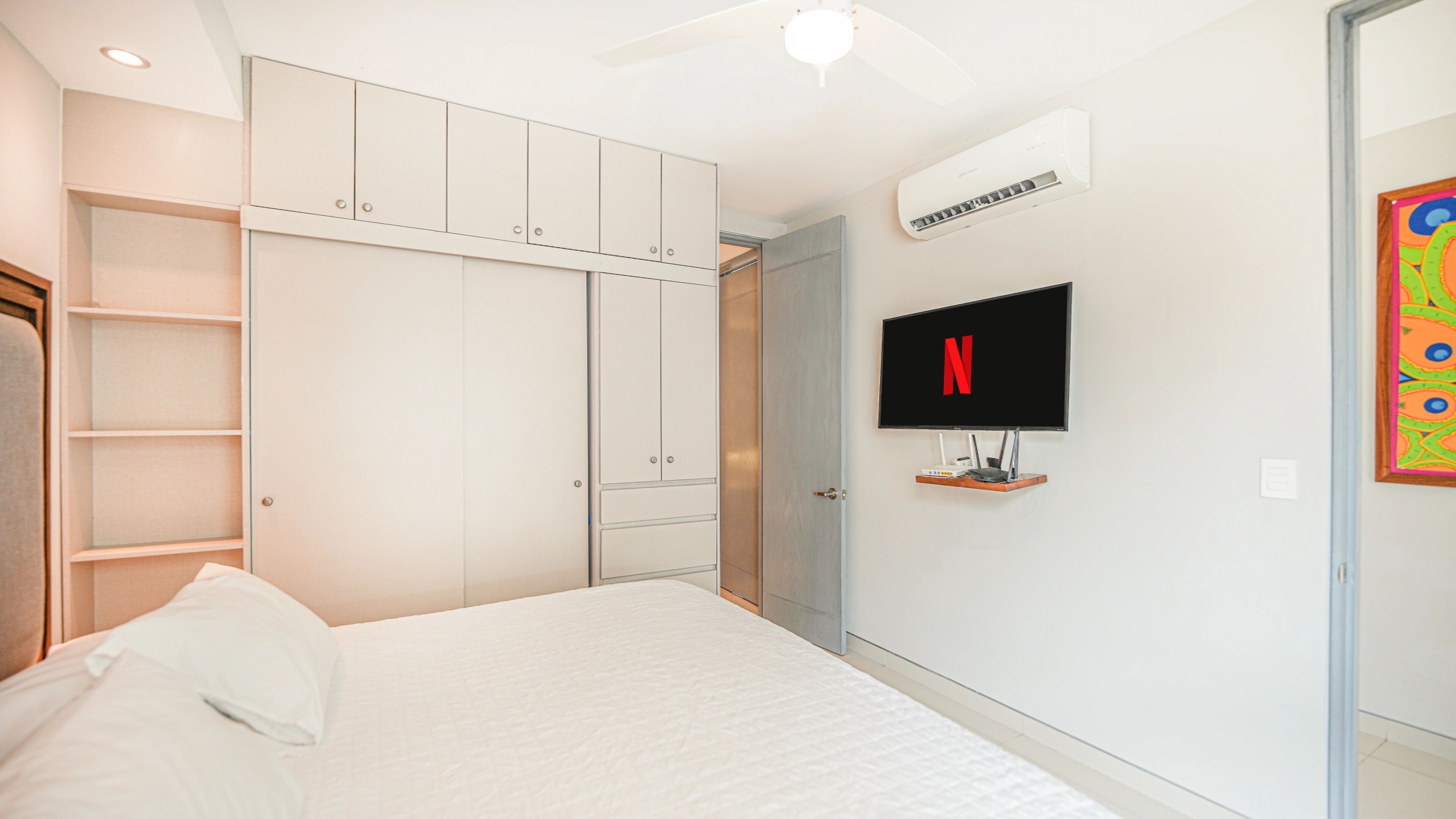 Ein Schlafzimmer mit Bett, Kleiderschrank, Wandfernseher und Klimaanlage.