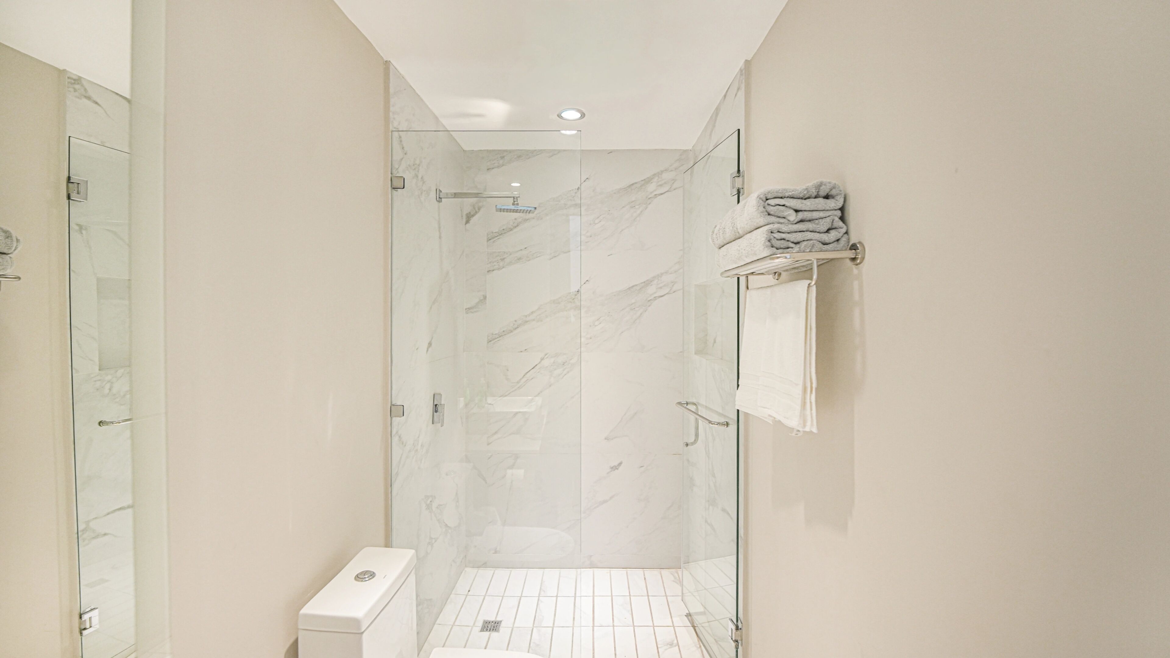 A modern bathroom with a glass shower enclosure, white marble tiles, and a toilet.
