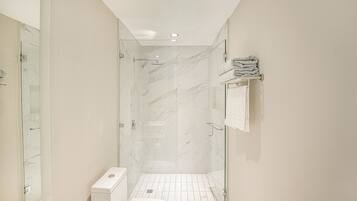 A modern bathroom with a glass shower enclosure, white marble tiles, and a toilet.