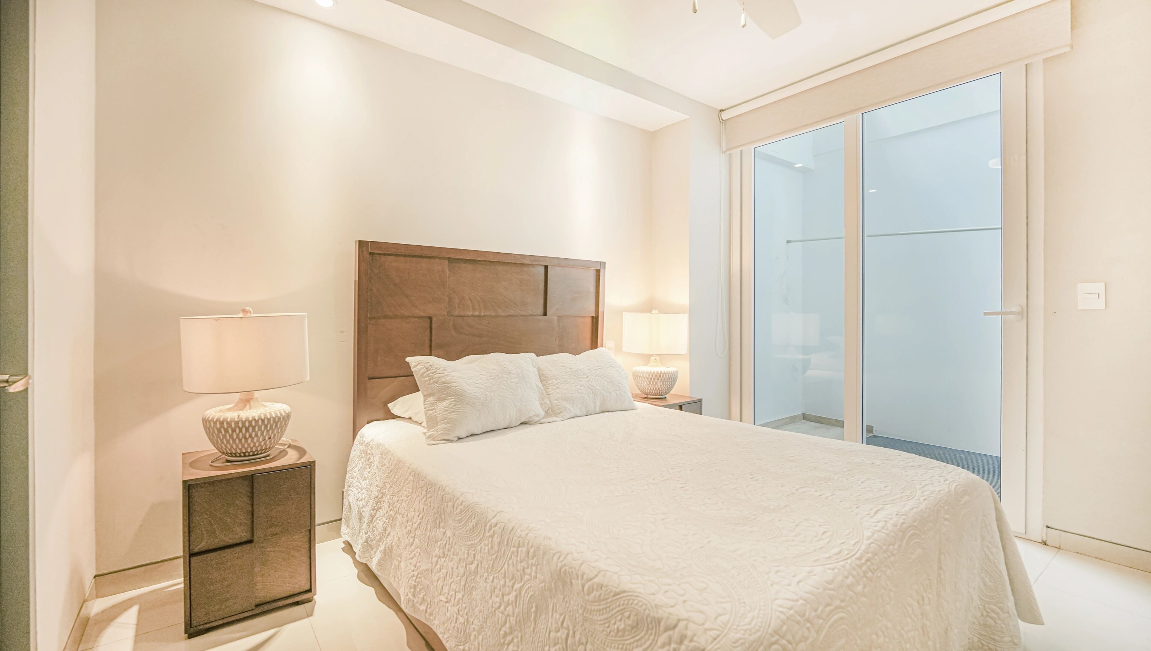Un dormitorio con una cama grande, dos mesitas de noche, un cabecero de madera y una puerta corrediza de cristal que da a un balcón.