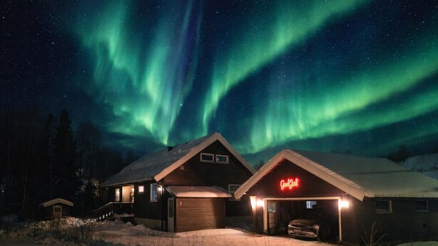 A cabin with a neon sign, under a night sky with aurora borealis.