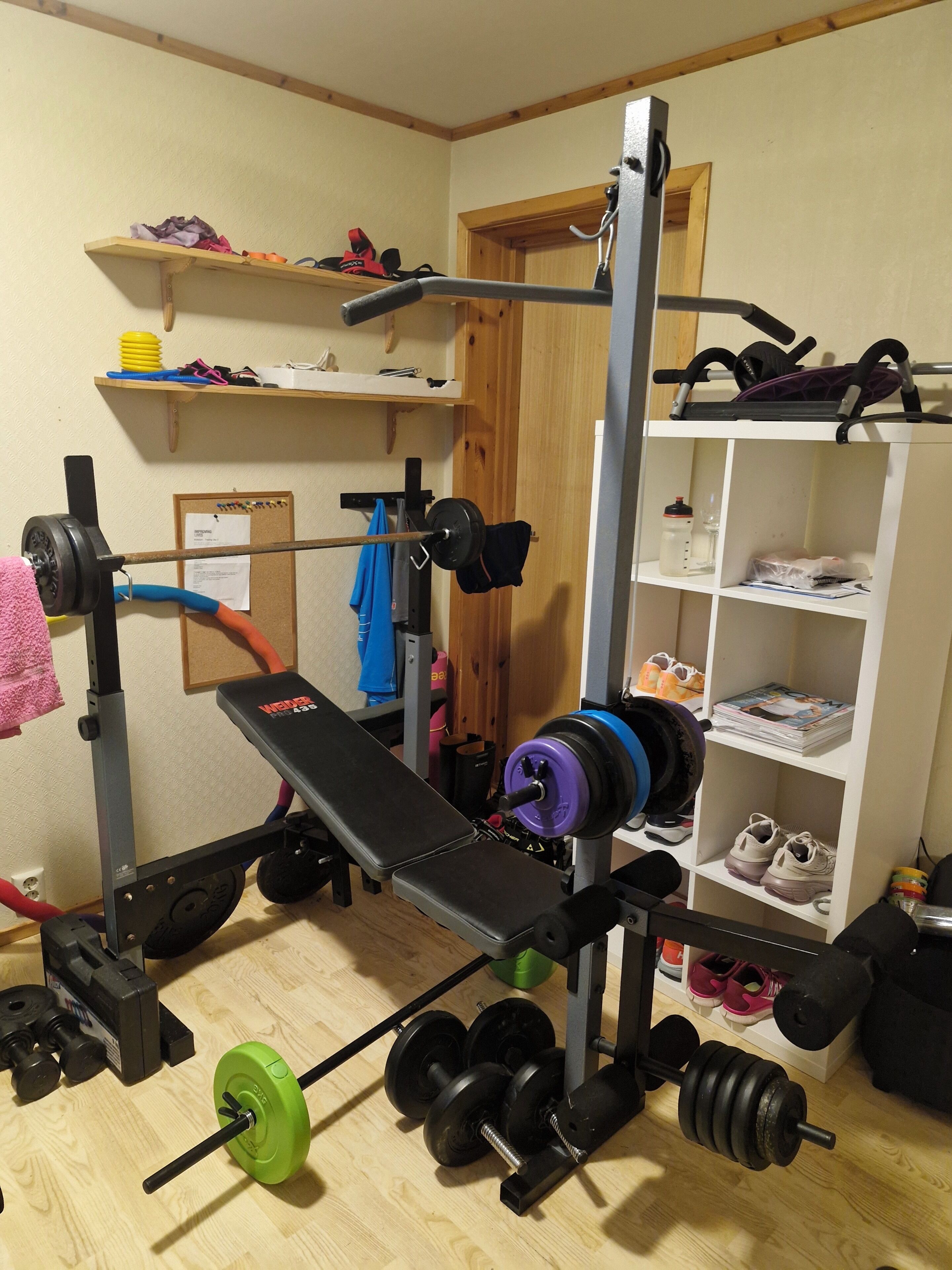 A home gym with a bench press, barbell, weight plates, and a squat rack.