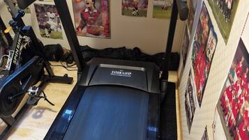Un tapis de course doté d’un écran numérique, entouré de divers objets de collection liés au sport.