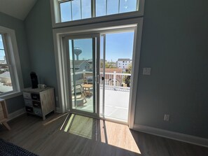 Ein Zimmer mit einer großen Schiebeglasdoor zu einem Balkon, einem Holzboden und einem weißen Schrank mit Schubladen.
