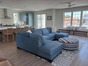 A modern living room with a sectional sofa, a dining area with chairs, a kitchen with blue cabinets, and large windows. - Brand new 4 bedroom 3 Bath house 2 blocks to the beach in charming Brigantine (Brigantine)