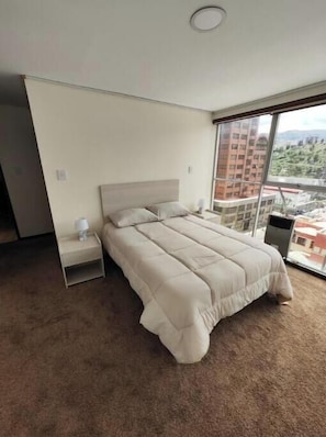 A bedroom with a large bed, a nightstand, a window with a city view, and a carpeted floor. - Comfortable apartment 2 D. The best location (La Paz)