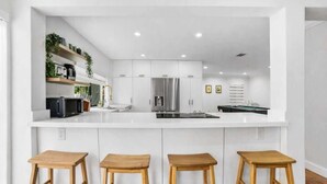 Una cocina moderna con armarios blancos, una isla central con taburetes y una mesa de billar.