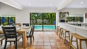 Una cocina moderna con una isla grande, comedor con sillas y vistas a una piscina.