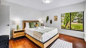 Un dormitorio con cama de madera, mesita de noche, ventana con vistas y alfombra blanca.