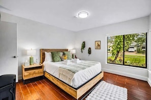 A bedroom with a wooden bed, a nightstand, a window with a view, and a white rug. - Pool * BBQ * Fire pit * Pool Table * TV room (Miami)