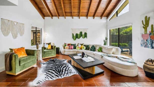 Un salón amplio con techo de madera, un ventanal grande y vistas al verdor exterior.