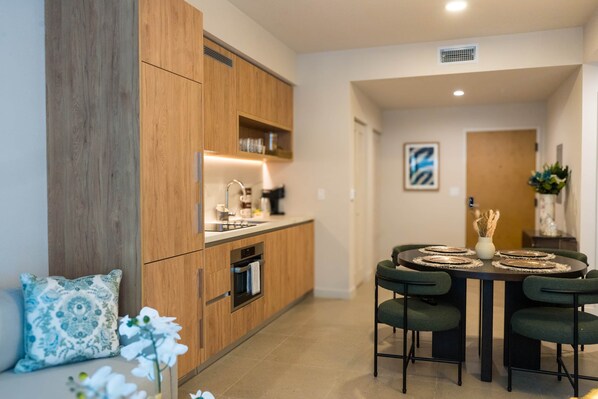 A modern kitchen with wooden cabinets, a built-in oven, and a dining area with a round table and chairs. - NEW Apt with PATIO in Downtown | CP Collection (Miami)