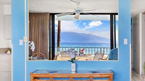 Une chambre avec vue sur la mer, un ventilateur de plafond, une table avec un vase de fleurs et une fenêtre avec des rideaux.