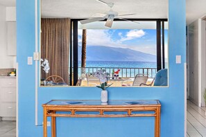 Ein Zimmer mit Meerblick, einem Deckenventilator, einem Tisch mit Blumenvase und einem Vorhangfenster.