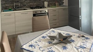 Eine Küche mit hellen Schränken, einem Edelstahl-Kühlschrank, einem Gasherd und einem Tisch mit blumigem Tischläufer.