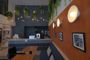 A modern interior with a reception desk, seating area, and wall-mounted lighting. - Yen Hostel & Smoothies Silom (Bangkok)