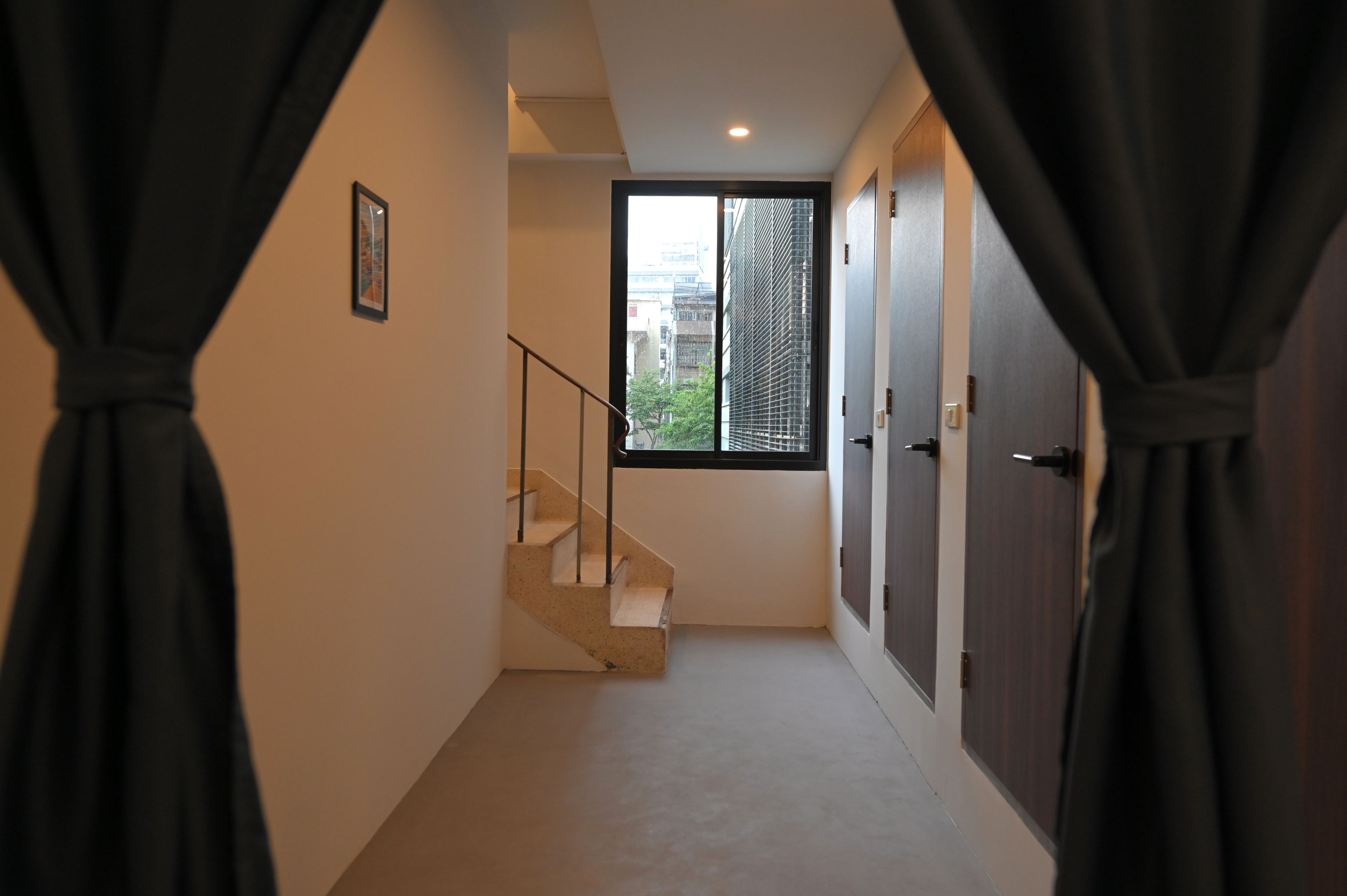 A corridor with a staircase leading to a window with a city view.