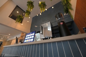 A coffee machine with a digital display, a menu board, and hanging greenery in a modern interior. - Yen Hostel & Smoothies Silom (Bangkok)