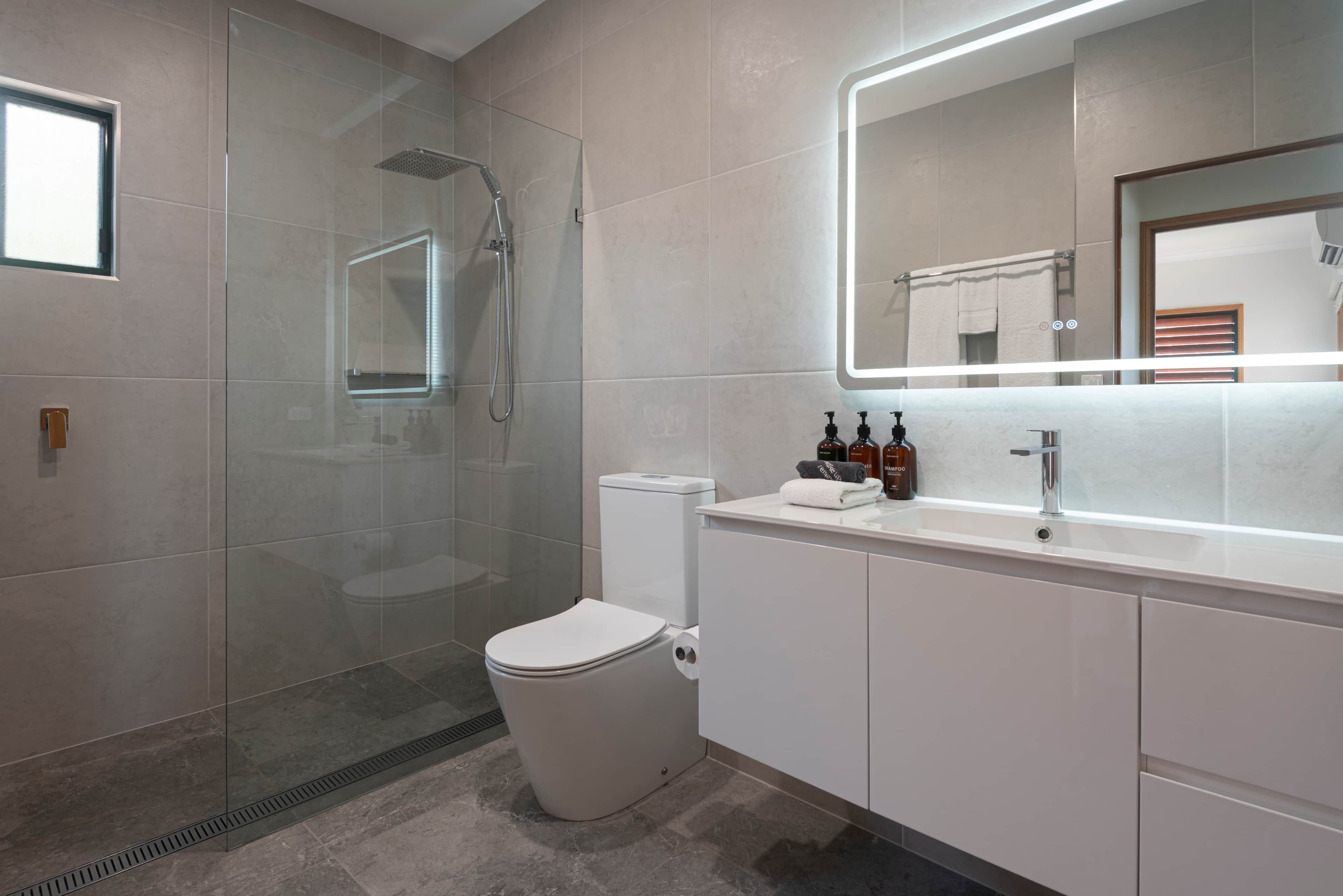 A modern bathroom with a glass-enclosed shower, a toilet, a vanity with a mirror, and a sink.