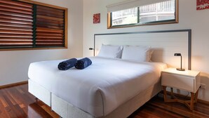 A neatly made bed with rolled towels, a bedside lamp, and a window with blinds. - Casuarina Cove 6 (Hamilton Island)