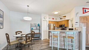 A compact kitchen with wooden cabinets, a stainless steel refrigerator, and a microwave. - Beacon Waves - Beach condo w/ Pool (Kill Devil Hills)