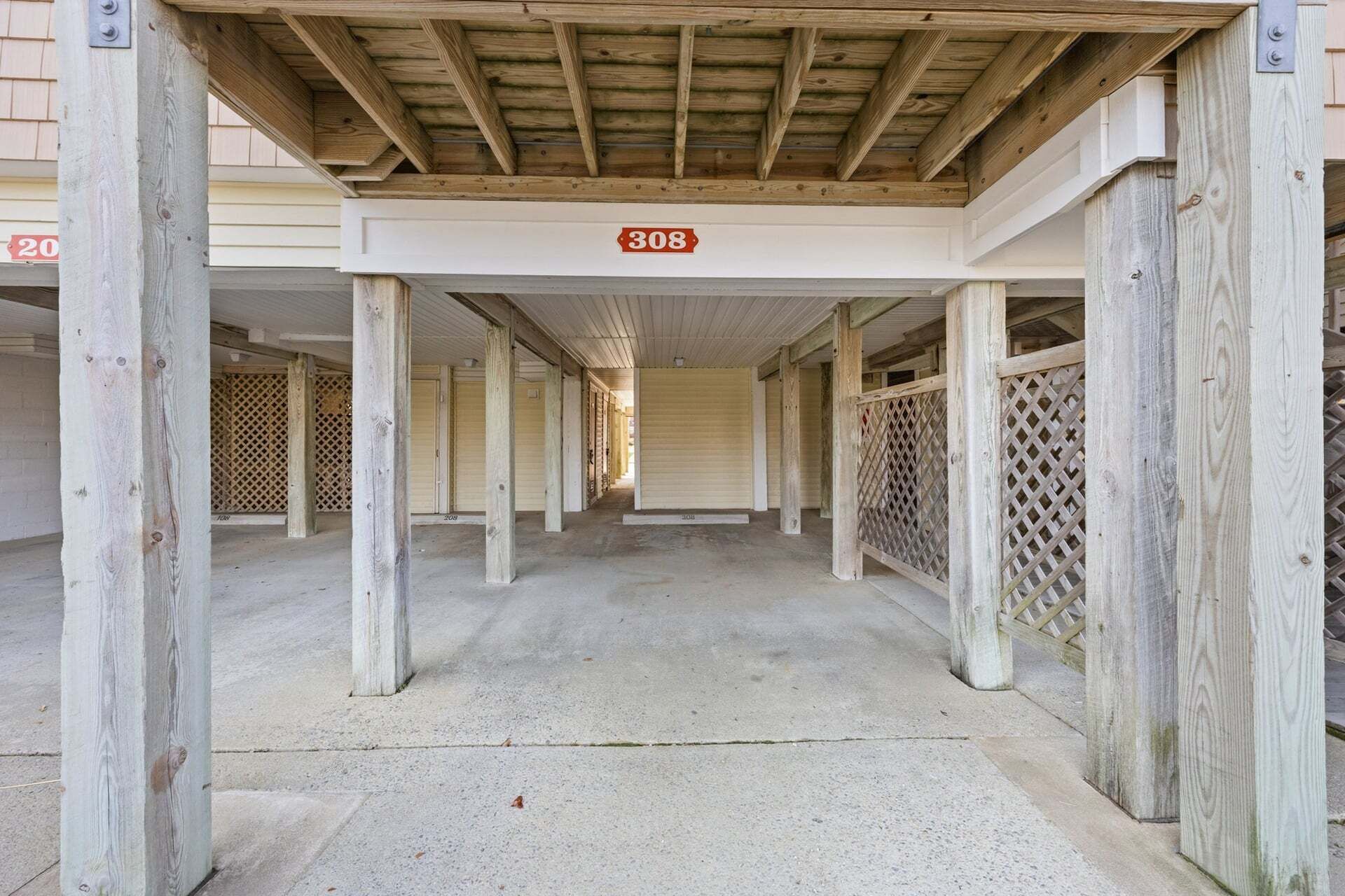 Un área de estacionamiento techada con columnas numeradas, piso de concreto y techo de madera.