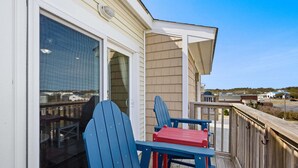 A wooden deck with two Adirondack chairs and a small table. - Beacon Waves - Beach condo w/ Pool (Kill Devil Hills)