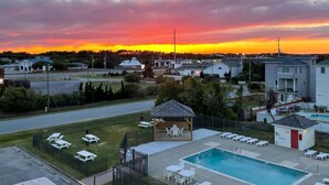 A residential area with a swimming pool, lounge chairs, and a gazebo. - Beacon Waves - Beach condo w/ Pool (Kill Devil Hills)