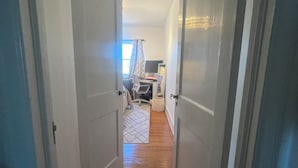 Um corredor estreito com piso de madeira que leva a um quarto com cama, escrivaninha e cadeira.