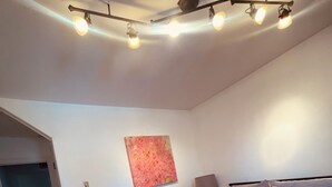 Quarto com uma cama grande, luminária no teto, quadro na parede e porta que dá para outro cômodo.