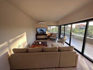 Ein modernes Wohnzimmer mit großem Fenster, einer Couch, einem Fernseher und einem Balkon.