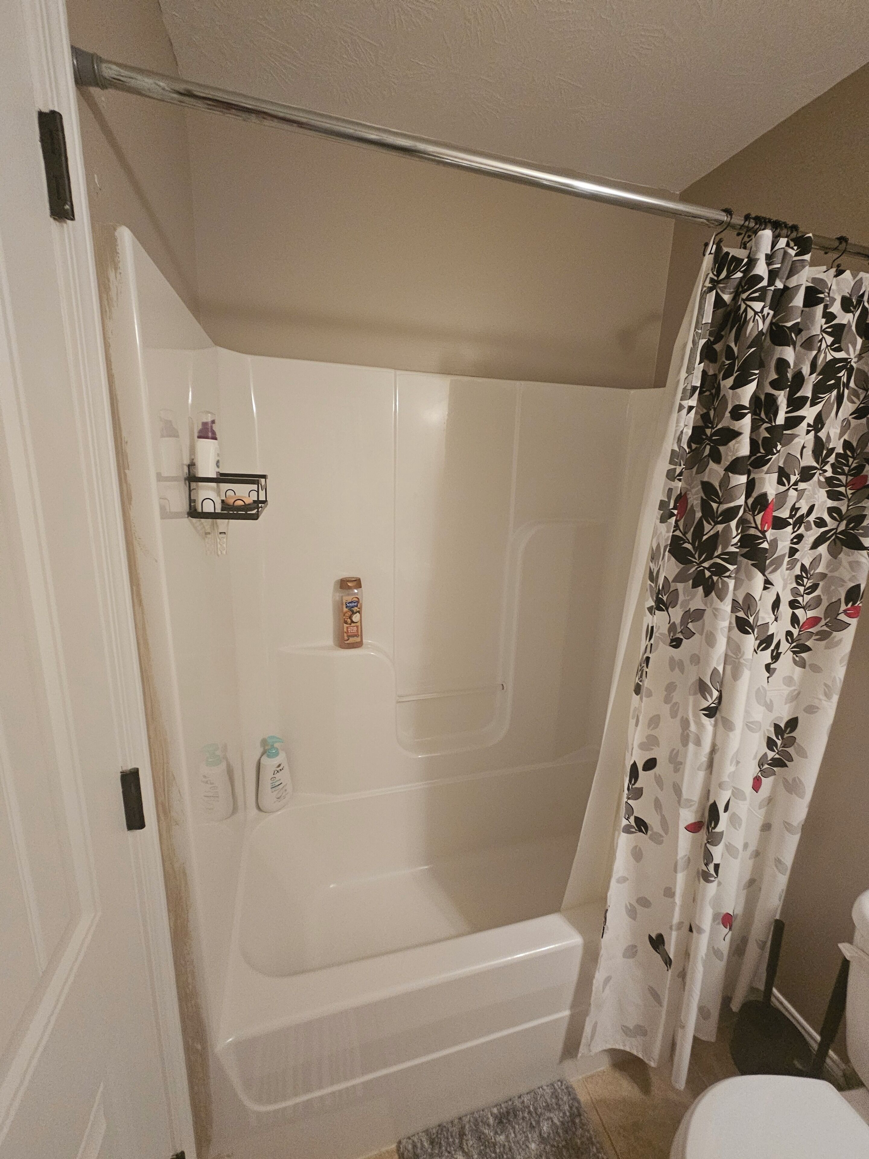 Un baño con ducha, inodoro y estante con artículos de aseo.