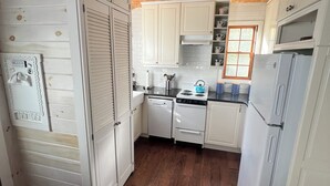 Une cuisine avec un plafond en bois, des armoires blanches, un lave-vaisselle, une cuisinière et un réfrigérateur.